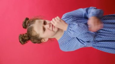 Boğazı ağrıyan genç kızın dikey görüntüleri stüdyodaki kırmızı arkaplan duvarında izole bir şekilde duruyor. Üzgün küçük çocuk boynuna dokunuyor. Sağlık sorunları kavramı