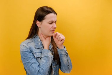 Hasta, mutsuz, genç, beyaz bir kadının portresi. Öksürük ve akciğerlerinde ağrı, grip belirtileri, kot ceket, sarı arka plan duvarında izole edilmiş pozlar.