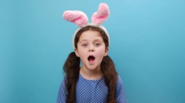 Sevimli Paskalya tavşanı kulakları takan, kolları açık ve gözleri açık, stüdyodaki mavi arka plan duvarında izole bir şekilde başarıya ulaşan oldukça mutlu bir genç kızın portresi. Kazanan konsept