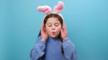 Sevimli Paskalya tavşanı kulakları takan, korkmuş ve şok olmuş genç kız portresi. Şaşırmış bir ifadeyle, korku ve heyecanla kameraya bakıyor. Stüdyonun mavi arka planında soyutlanmış poz veriyor.