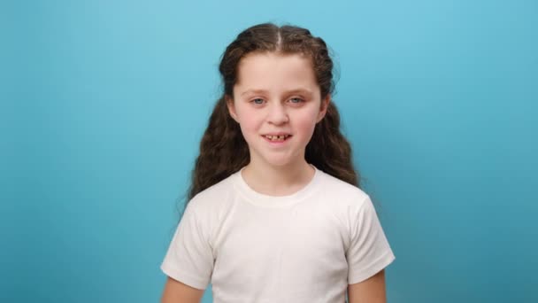 可爱的小女孩的画像 恭恭敬敬地望着相机 爱国的孩子 身穿白色休闲装 在工作室的浅蓝色背景墙上摆出隔离的姿势 — 图库视频影像