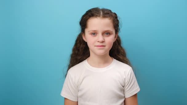 スタジオの青色の背景の壁の上に隔離された白いTシャツを身に着けている電話で電話をかけるかわいい少女の子供の肖像画 — ストック動画