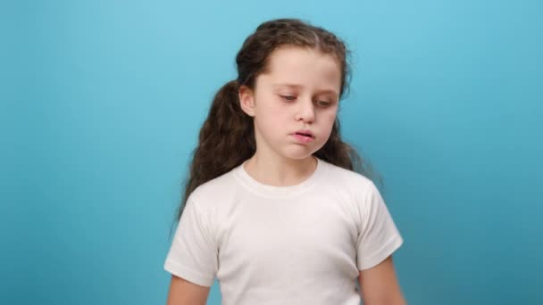 心烦意乱的小女孩的画像靠在手上 看上去很沮丧 表情冷漠的孩子没有精力 穿着白色的T恤 在演播室的蓝色背景墙上显得孤立无援 — 图库视频影像