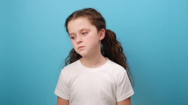 不幸な少女の肖像画 ジェスチャーに疑問を抱き 答えを知らず 疑問を表明し 白いTシャツを着てスタジオの青い色の背景の壁の上に隔離された — ストック動画
