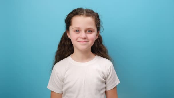 自分自身を指摘する笑顔の小さな少女の子供の肖像画 自慢し 勝利を喜び 功績を誇り 白いカジュアルなTシャツを着てスタジオの青い色の背景の壁の上に隔離された — ストック動画