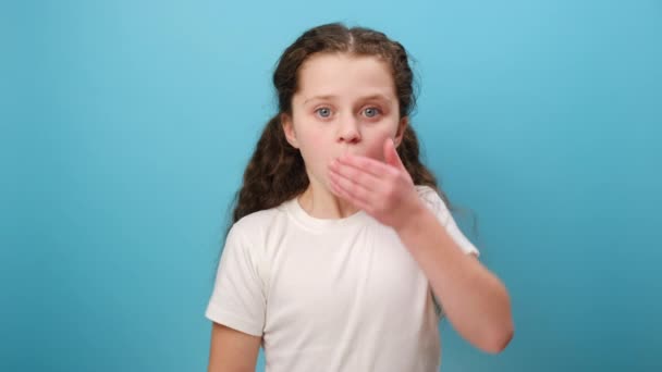 忧心忡忡的小女孩用手捂着嘴 不敢说秘密 害怕说话 穿着白色T恤衫 在演播室里与浅蓝色背景墙隔离的画像 — 图库视频影像