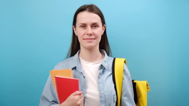 身穿衬衫 背着书包 头戴黄色箭头 快乐可爱的女学生的肖像 在工作室的蓝色背景墙上显得孤立无援 高中教育 — 图库视频影像