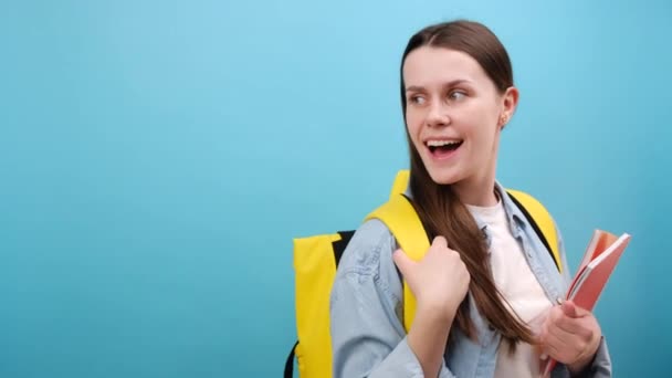 身穿衬衫 背着背包的年轻可爱女生的侧面视图 在蓝色的工作室背景上与复制空间隔离 高中学院教育的概念 — 图库视频影像