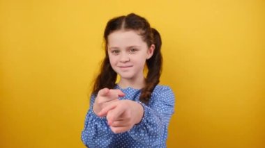 Üzerinde mavi işaret parmağı olan 8-9 yaşındaki sevimli küçük kız çocuğunun portresi. Stüdyodaki sarı renkli arka plan duvarına izole edilmiş bir poz veriyor. Çocukluk yaşam tarzı konsepti