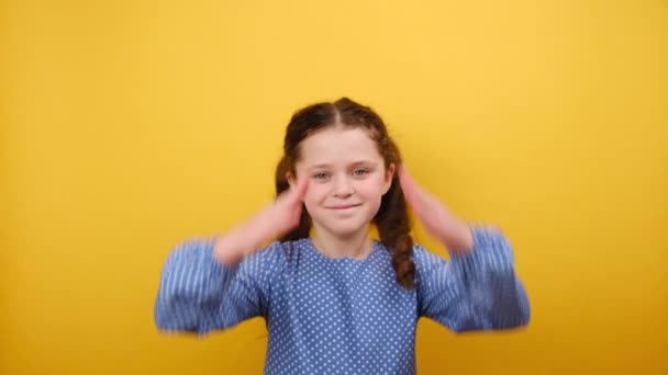 青いドレスを着ているかわいい笑顔の少女8 9歳の肖像画は 屋根のように頭の上に折られた手を保持し スタジオの黄色い背景の壁に隔離されています 子供時代のライフスタイルコンセプト — ストック動画
