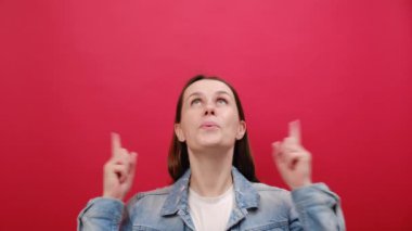 Kot ceketli, mutlu genç bir kadının portresi çalışma alanı fotokopi alanını işaret ediyor, reklam alanı, stüdyo odasındaki kırmızı duvarın arkasında izole edilmiş poz veriyor.