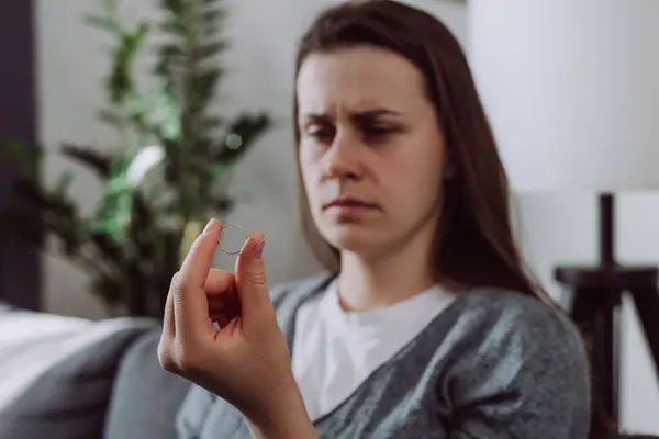 stock image Unhappy sad female stressed with relationships end or breakup. Selective focus of worried upset young woman holding wedding ring think of marriage dissolution or divorce having family problems