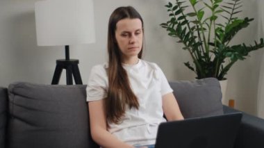 Modern oturma odasındaki rahat kanepeye yerleşmiş, düşünceli arama fikirleri olan, müşteriye karşılık gelen, kablosuz teknoloji ve internet bağlantısı kullanarak işi çözen serbest çalışan bir kadın.
