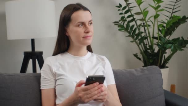 Όμορφη Νεαρή Γυναίκα Που Χρησιμοποιεί Κινητό Τηλέφωνο Κάθεται Στον Καναπέ — Αρχείο Βίντεο