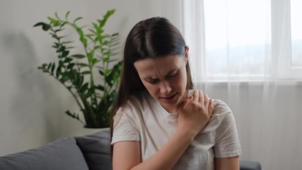 年轻的高加索女人按摩揉搓僵硬的脖子酸痛紧张的肌肉疲倦了 感觉关节酸痛一个人坐在客厅的沙发上 纤维肌痛的概念 — 图库视频影像