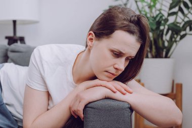 Mutsuz, sinirli, genç, beyaz bir kadın evde tek başına oturuyor üzgün, yorgun ve endişeli, akıl sağlığında depresyon geçiriyor, suçluluk hissediyor, zor bir karar veriyor.