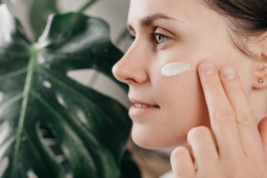 Yüzüne krem sürerek yeşil canavarın yanında duran güzel, gülümseyen beyaz bir kadının güzel portresi. Kusursuz cilde önem veren gülümsemenin tadını çıkar. Cilt bakımı kavramı