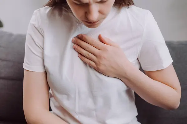 Ungesunde Junge Frau Sitzt Auf Sofa Mit Atembeschwerden Herzschmerz Berührt lizenzfreie Stockfotos