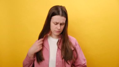 Hasarlı saçlara dokunan mutsuz genç bir kadının portresi, saç dökülmesinden endişe eden üzgün bir kız kameraya bakıyor hormonal dengesizlikten muzdarip, sarı stüdyo arka planında izole edilmiş.