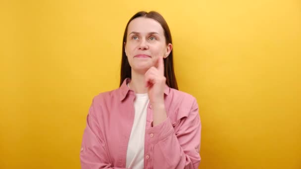 年轻女子的画像 表情严肃而聪明 思考着答案 带着伟大的新想法举起食指 穿着粉色衬衫 在黄色的工作室背景墙上显得孤立无援 — 图库视频影像