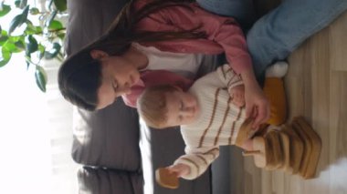 Mutlu dadının güzel bir çocukla modern ve rahat bir evde vakit geçirdiği dikey video. Sevgi dolu genç bir anne, tahta küplerle sevimli bir çocukla oynuyor. Çocuk gelişimi, oyun zamanı kavramı