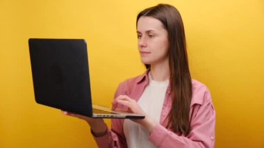 Çok şaşırmış genç bir kadın ofis çalışanının portresi büyük gözleri ve ağzı açık bir şekilde dizüstü bilgisayara bakıyor, kutlama zaferi, stüdyoda sarı renkli arka planda izole edilmiş poz veriyor.