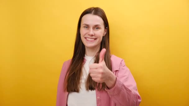 笑顔の魅力的な若いブルネット女性の肖像画は ジェスチャーのように親指を示し カメラを見て 推奨サービス スタジオの平らな黄色の背景の壁の上に隔離されたポーズ — ストック動画