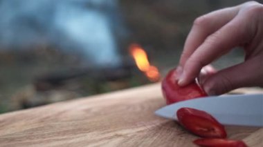 Kadın ellerini doğaya şenlik ateşinin yanında tahta tahtada taze kırmızı biber keserek kapat. Kesme tahtasında biber kesmeye hazırlanıyorum. Dışarıda yemek pişirmek. Piknik ve macera konsepti