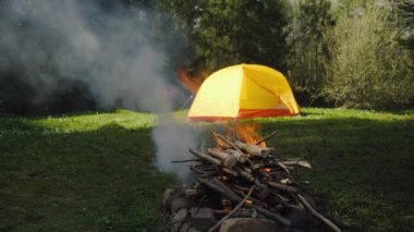 Akşam karanlığında kamp ateşini kapatın. Sarı çadır ve bahar ormanlarına karşı. Akşam vakti havada kıvılcımlar uçuşan turist şenliği ateşi. Dışarıdaki yaşam tarzları için ilham verici bir kamp yeri.