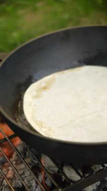 Şenlik ateşinde etli Meksika tacoları pişirmenin dikey videosu. Kampta kahvaltı hazırlıyorum. Yemek, seyahat ve seyahat tutkusu.