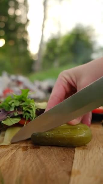 暖かい春の日没の間に森のボンファイア近くの木製板にナイフを切った女性の手の縦の映像 屋外で料理する 食べ物 休暇の自然コンセプト — ストック動画