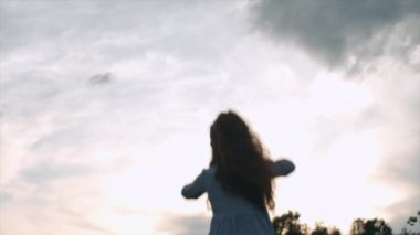 Yaz günbatımında arka planda bulutlu gökyüzünde mutlu küçük kız çocuğu silueti. Çocuğun sağlığı ve mutluluğu için el kaldırılması ve dua edilmesi. Umut, inanç ve iyimserliğin sembolü.