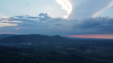 Yüksek yeşil ormanın üzerindeki renkli günbatımının sinematik drone görüntüsü. Yaz mevsiminde dağ havası, bulutlu gündoğumunda güzel destansı manzara. Açık hava macera konsepti