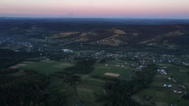 Akşam saatlerinde kırsal kesime yaklaşan orman, evler ve tarlalar arasındaki hava aracı görüntüsü. Yaz ya da bahar aylarında kayan tepelerin panoramik manzarası
