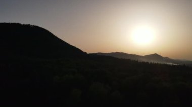 Yaz mevsiminde sıcak günbatımında muhteşem dağların havadan görüntüsü. Gökyüzündeki parlak güneş diski yavaşça dağların tepesine çıkar. Doğa konsepti