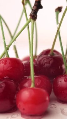 Beyaz stüdyo arka planında su damlaları olan olgun kirazların dikey videosu. Seçici odaklanma. Kırmızı kiraz hasadına yakın. Kirazlardan yemek ve meyve suyu