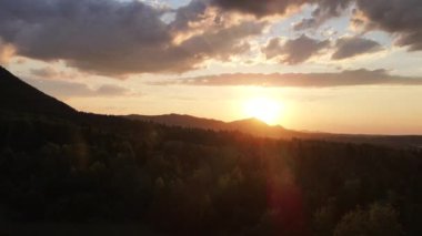 Dağların havadan çekilmiş görüntüleri ve yaz mevsiminde gün batımının ya da güneşin doğuşunun inanılmaz sıcaklığı. Dağ sırasının yeşil orman yamaçları silueti. Gökyüzündeki parlak güneş diski yavaşça dağların tepesine çıkar.