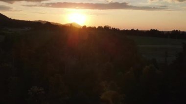 Dağların havadan görünüşü ve yaz mevsiminde sıcak gün batımı. Dağ sırasının yeşil orman yamaçları. Gökyüzündeki parlak güneş diski yavaşça dağların tepesine çıkar. Doğa konsepti