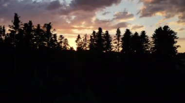 Güneş doğarken heybetli ormanın silueti ve güzel renkli gökyüzü. Gökyüzündeki parlak güneş diski yavaşça batıyor. Dağların havadan görünüşü ve yaz mevsiminde sıcak gün batımı.