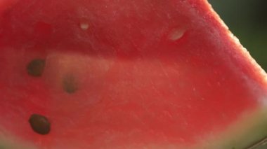 Dönüşümlü taze dilimlenmiş karpuzu kapat. Sıcak yaz günbatımında arka planda yeşil bir tabakta sulu karpuz dilimler. Seçici odak