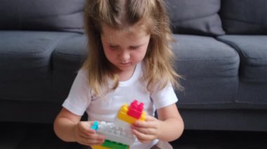 Meraklı küçük kız, renkli plastik tuğlalarla oynuyor. Evdeki kanepenin yanında oturuyor. Çocuk gelişimi, bebek bakıcılığı, hafta sonları ev konseptinde boş oyunlar