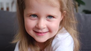 Kameraya bakıp gülümseyen sevimli, pozitif küçük kız çocuğunun portresini yakından çek. Mutlu şirin kız evdeki rahat koltukta oturup çocukluğun tadını çıkarıyor, keyifli bir ruh hali içinde.