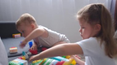 Çocuklar evdeki rahat koltukta oturan müteahhit küpleriyle oynuyorlar. Sevimli erkek bebek ve küçük kız anaokulundaki kanepede renkli oyuncak blokları oynuyorlar. Aile öncesi eğitim konsepti. Seçici odak