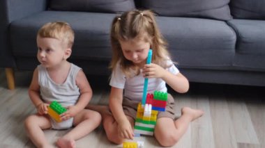 Çocuklar renkli oyuncak bloklarıyla oynuyorlar. Bebek ve küçük kız oyuncaklardan kule yapıyorlar. Kardeşler için eğitici ve yaratıcı oyuncaklar ve oyunlar. Çocuklar odalarında gökkuşağı tuğlalarıyla