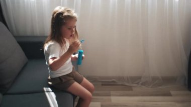 Evdeki rahat koltukta oturup sabun köpüğü üfleyerek eğlenen komik, güzel, küçük bir kız çocuğu. Dişsiz, oynak bir çocuk sabun köpüğü üflüyor. Çocukluk kavramı