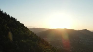Sıcak günbatımında inanılmaz dağların hava görüntüsü. Dağ sırasının orman yamaçları. Güneşin parlak diski yavaşça dağların tepesine çıkar. Dramatik gün doğumu gökyüzü arkaplanı
