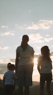 Arka plandaki dağlara uzanan mutlu çocukların dikey videosu. Kardeşlerin zaferi kırsal alanda gün batımında el kaldırıyor, doğada dinleniyor. Özgürlük duygusu ve uçma düşüncesi