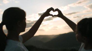 Arka planda elleri ile kalp yapan çocukların silueti inanılmaz günbatımı. İçinde gün doğumu olan ellerden kalp gösteren tatlı kızlar. Tatil, turizm ve tatil konsepti. Yaz tatili