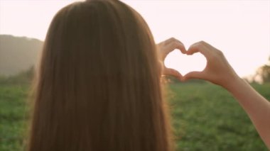 Genç bir kadının kalp şeklinde el ele tutuşup gün batımında dağlarda güneşin batışını izlemesi. Yaz rüyası kavramı. Gün doğumunda sahalarda özgürlük. Parkta tatlı bir kız.