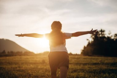 Arka plandaki dağlarda ve gün batımında gökyüzünde koşan küçük kızın seçici odağı. Çocuk kollarını bir uçağın kanatları gibi kaldırarak koşuyor, çocukluk hayali tatili. Çocuk rüyası, uçak pilotu